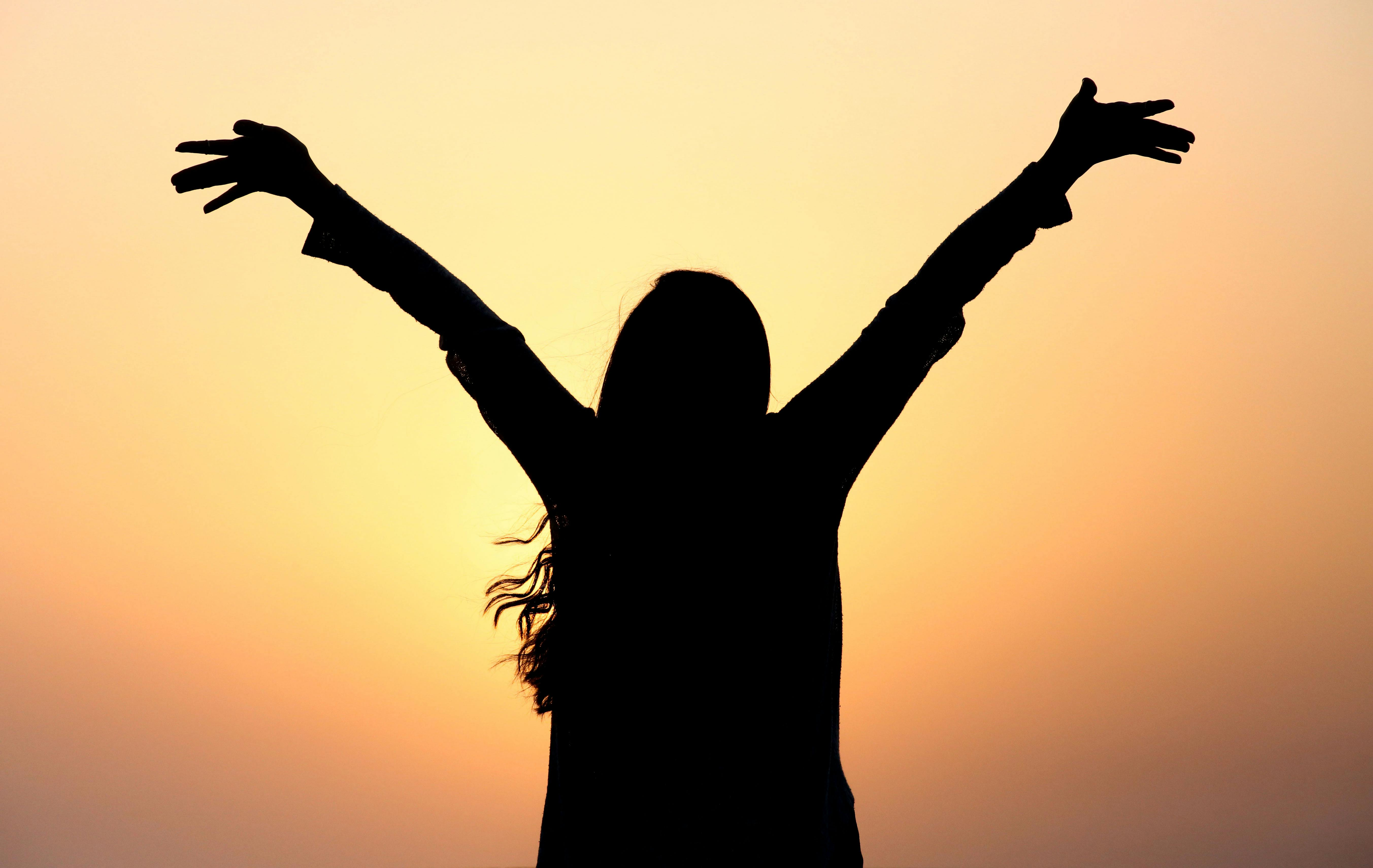 Student standing outdoors with arms open in surrender